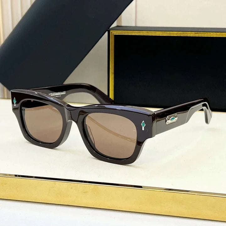 A pair of stylish black square retro sunglasses with brown tinted lenses, resting on a cream-colored surface. The arms feature turquoise diamond-shaped details near the hinges and offer UV400 protection.