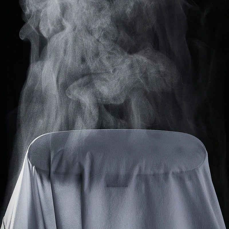 A close-up of a lightweight white shirt draped over a surface with steam rising from it against a black background, suggesting the shirt is being ironed or steamed.