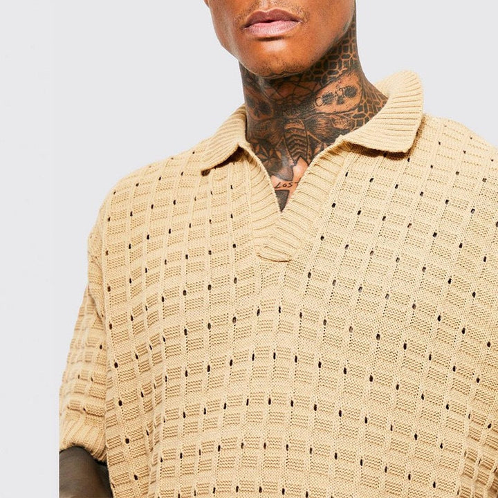 A person with neck tattoos wears a beige, short-sleeved summer shirt with a collar and open neckline, featuring a breathable knit design. Shown from the shoulders up against a plain background.