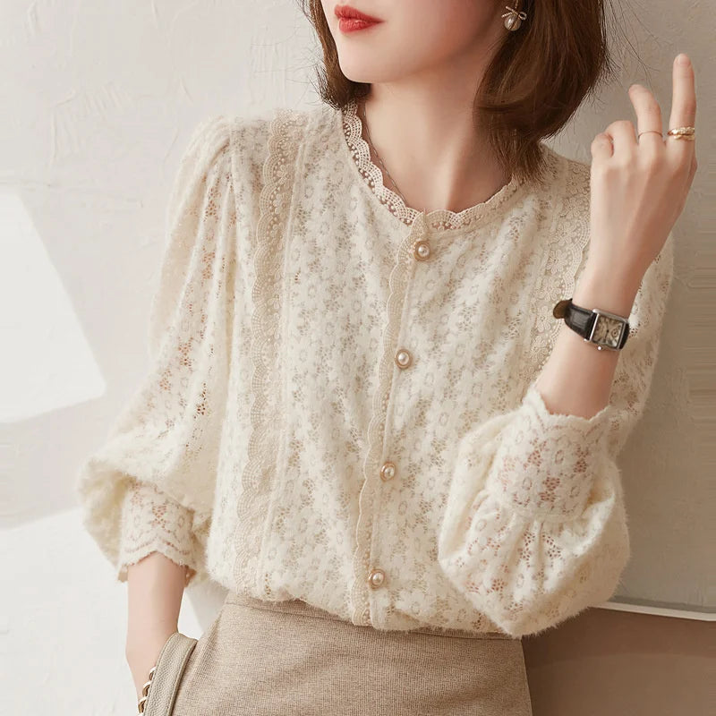 A woman wears an ivory lace blouse with vintage pearl buttons and puffed sleeves, paired with a beige skirt. She accessorizes with a watch, ring, earrings, and has shoulder-length brown hair.