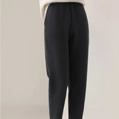 A person wears high-waisted, loose-fitting black pants with a slim tailored leg and ultra soft insulation, paired with a white, long-sleeve top. The background is plain and neutral. The upper body and face are not visible.