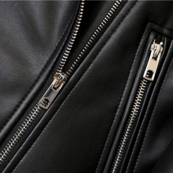 Close-up of a black leather jacket featuring two silver zippers and visible stitching, highlighting the texture of the leather, details of the metal zipper teeth and pulls, and an adjustable waist belt.