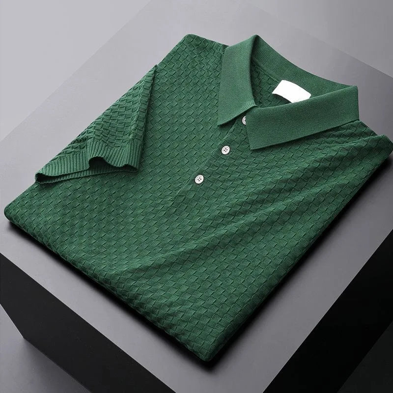 A neatly folded dark green polo shirt with a textured, waffle jacquard diamond-patterned fabric, three buttons, and a classic collar, displayed on a black and gray surface.