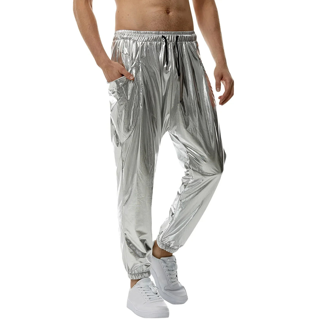 A person wearing shiny silver jogger pants made from lightweight metallic fabric with an elastic waistband and tapered leg, paired with white sneakers, stands against a white background with one hand in their pocket.