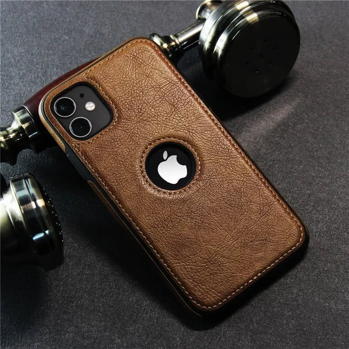 A smartphone in a slim protective, luxury leather phone case with a circular cutout for the Apple logo rests on a dark surface beside metallic salt and pepper shakers. The case is also wireless charging compatible.