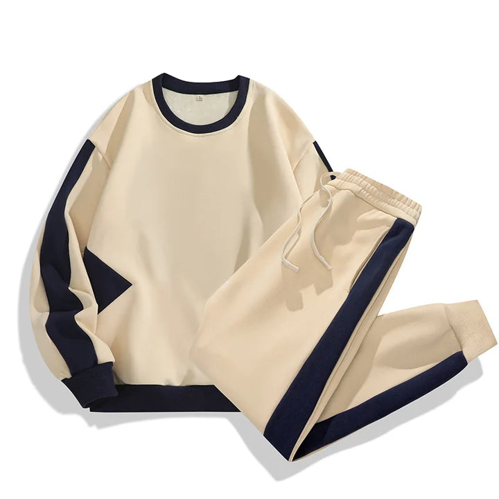 A beige sweatshirt and matching jogger pants in a relaxed fit, featuring dark blue accents on the sleeves, sides, and cuffs. Crafted from a soft cotton blend, this casual loungewear set is laid out on a white background.
