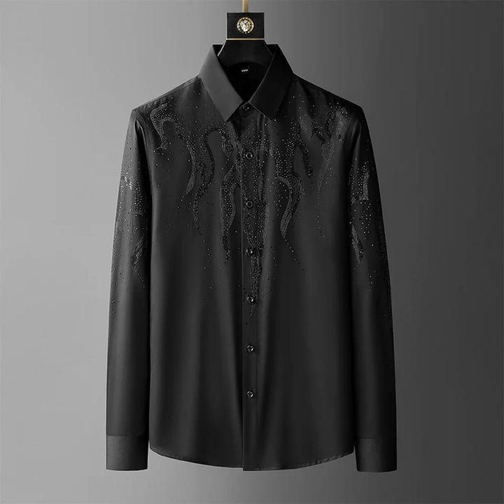 A black tailored fit button-up shirt with a collar, featuring subtle, glossy flame-like patterns and scattered rhinestones on the chest and shoulders, hangs against a plain gray background.