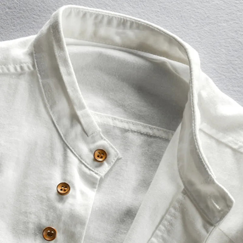 Close-up of the collar and upper front part of a Japanese inspired overshirt with a mandarin collar and brown buttons, crafted from 100% cotton, laid flat on a light-colored surface.