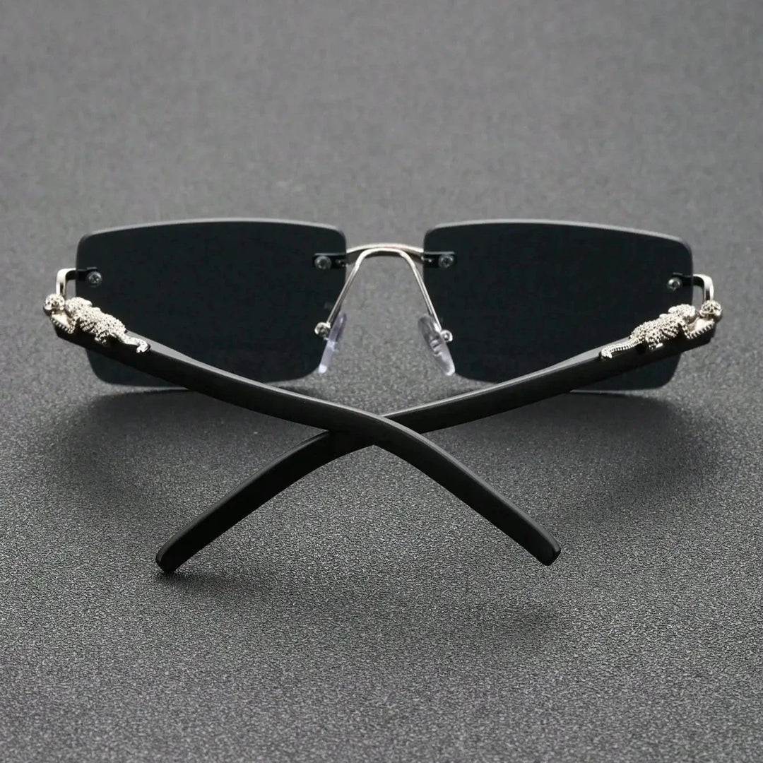 Rimless black sunglasses with UV400 protection, dark lenses, and silver accents on the temples, displayed with the arms crossed on a textured dark surface.