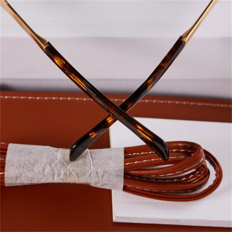 Close-up of two brown tortoiseshell eyeglass arms crossed over each other, resting on a coiled brown leather strap, with a white background—perfect for those who appreciate vintage-inspired sunglasses and timeless Italian style.