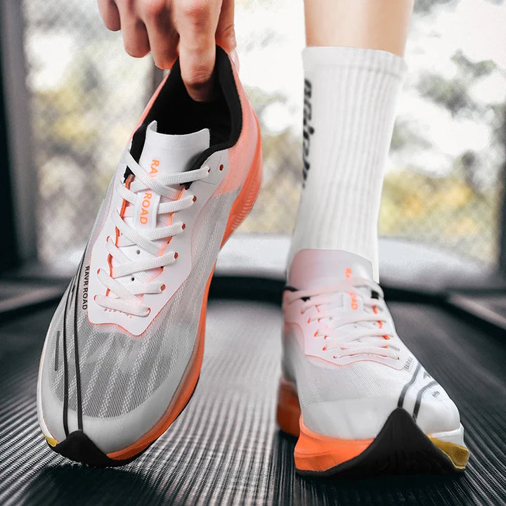 A person wearing white athletic shoes with orange soles and white socks stands on a treadmill, adjusting the heel of one shoe. The shoes feature a sleek, modern design with lightweight construction for maximum comfort.
