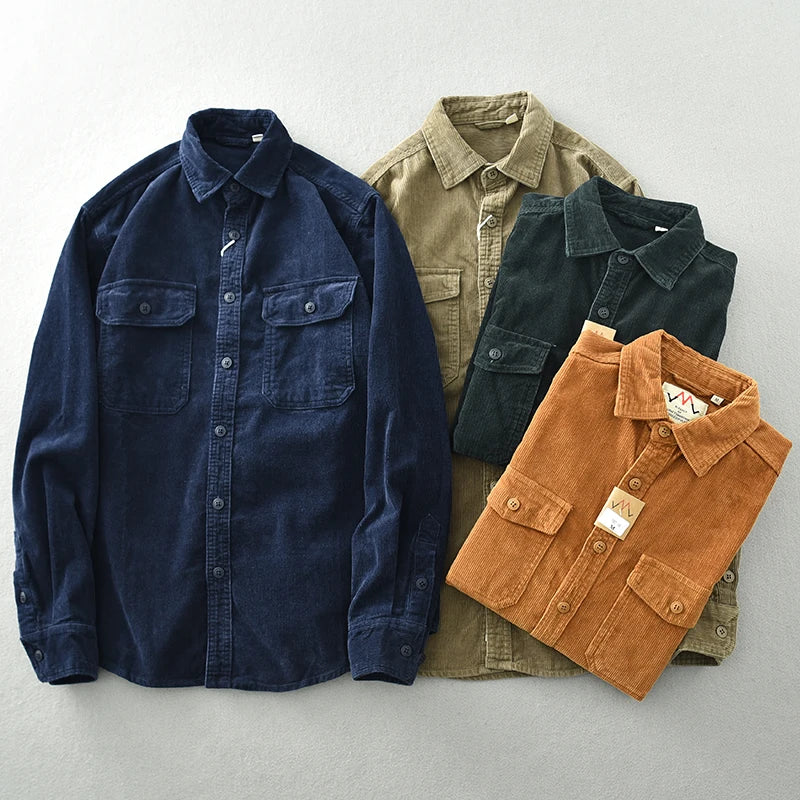 Four button-up shirts, crafted from heavyweight cotton with classic corduroy detailing, are neatly arranged on a light surface in navy blue, olive green, dark green, and brown. Each features a collar and two chest pockets with buttoned flaps.