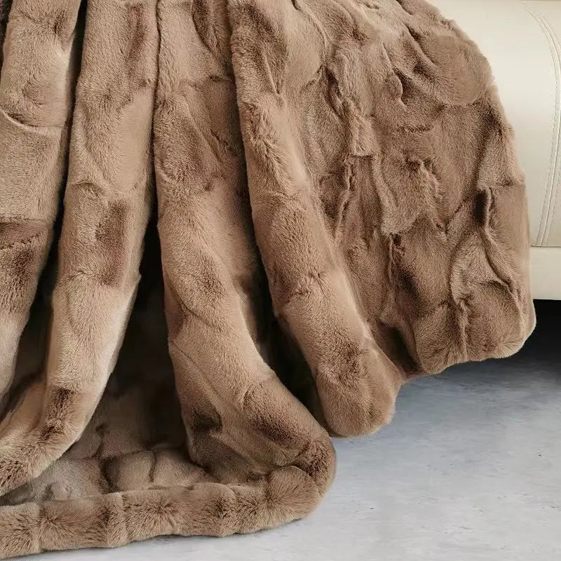 A plush faux fur blanket in soft brown is draped over the edge of a beige sofa, with part of the cozy throw pooling onto a light gray floor.