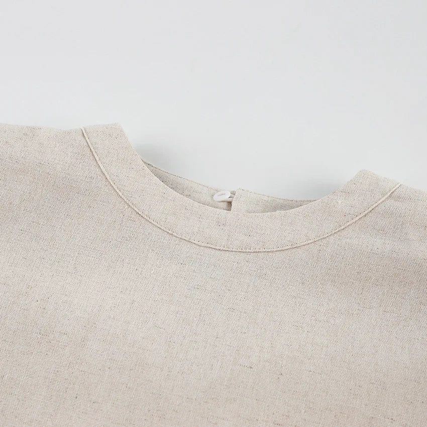 Close-up of the neckline of a beige, Belgian Linen Blend shirt with a textured, woven fabric, featuring a round collar and a small button loop closure at the back.