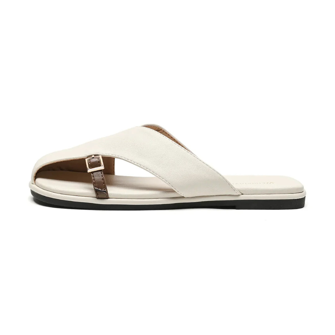 A white leather slide with a flat black sole, featuring a wide crisscross strap and a small brown buckle on one side—perfect for elevating your summer wardrobe in chic slides style, shown in a side profile view.