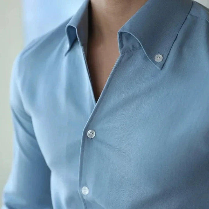 A person wearing a light blue, wrinkle resistant shirt with an open collar, revealing part of their neck and upper chest. The focus is on the slim fit shirt’s style and fabric, not the face.