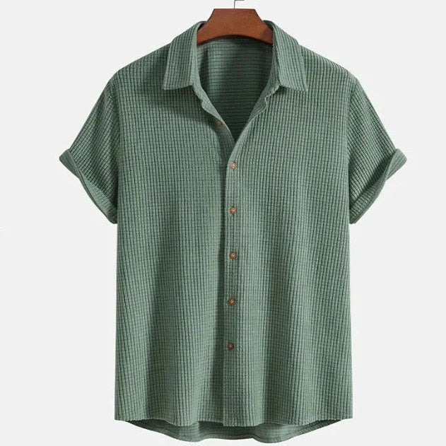 A short-sleeved, light green textured Bayside Shirt made of breathable cotton with a collar, displayed on a wooden hanger against a plain light background—perfect for your summer wardrobe.
