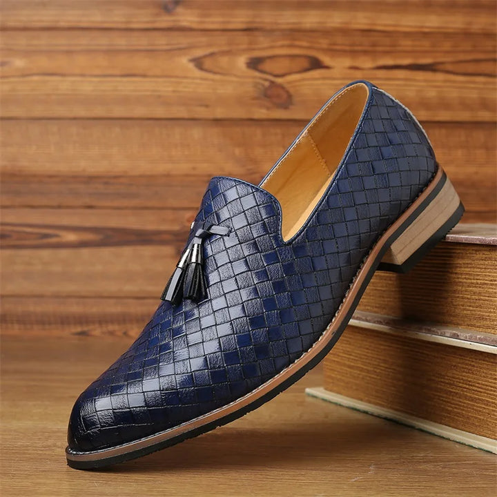 A single blue woven leather loafer with tassels sits on a wooden surface, featuring a tan lining and a light brown sole with dark trim—a fine example of real leather shoes and luxury footwear.