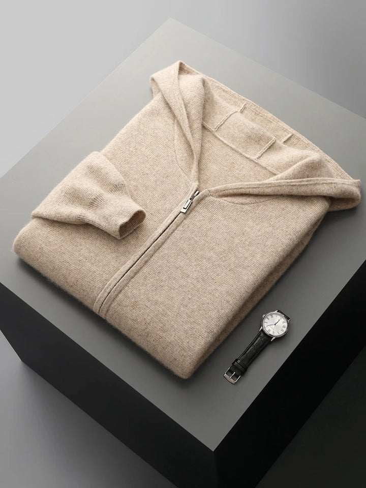 A beige zip-up hoodie neatly folded on a gray surface, with a black leather strap wristwatch placed beside it—perfect for pairing with your favorite autumn winter cardigan.