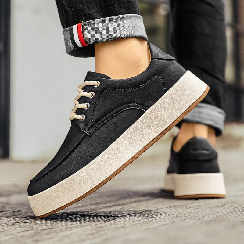 A person wearing black breathable walking shoes with thick white soles stands on a sidewalk. The jeans are cuffed, revealing the inner seam detail. The focus is on the comfortable footwear.