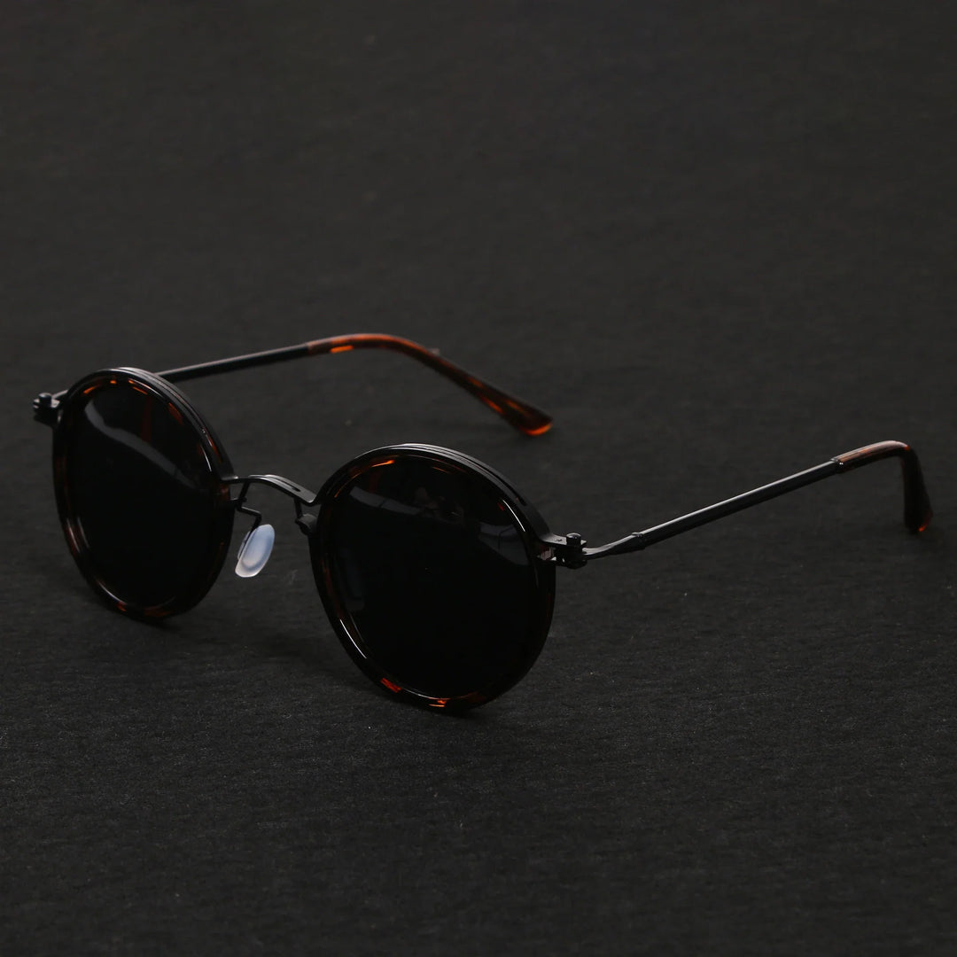 A pair of round, dark-lensed Ruby Ray Sunglasses with thin, black metal arms and tortoiseshell details offers stylish UV400 protection, resting on a plain black surface.
