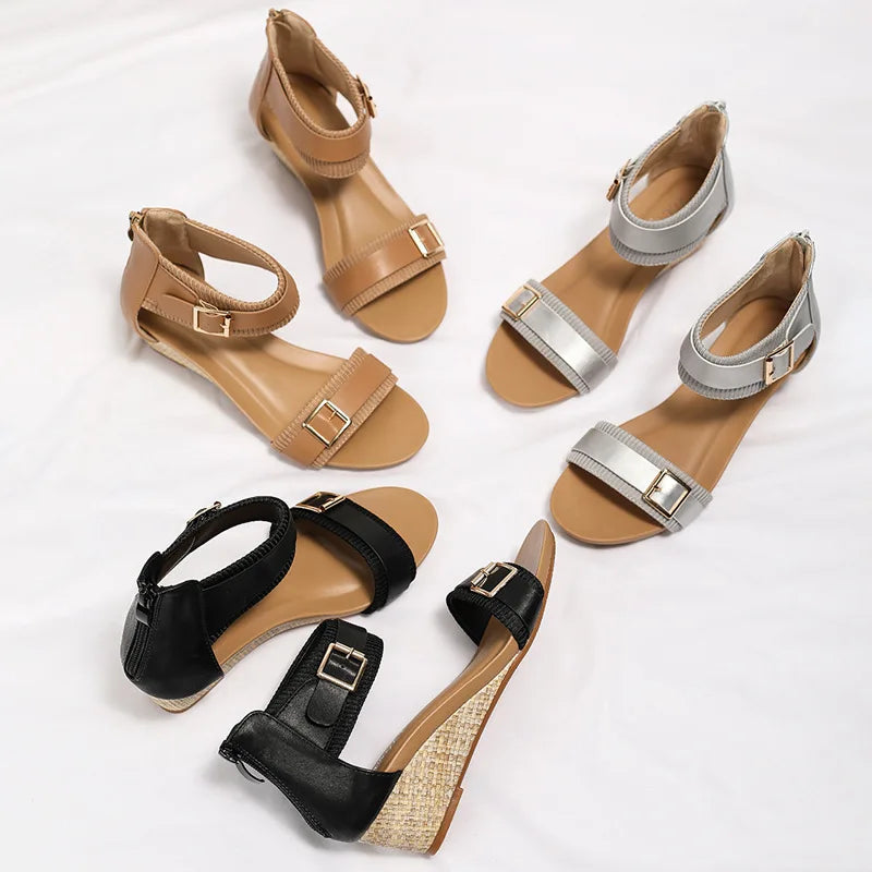 Three pairs of women's sandals are displayed on a white surface in tan, silver, and black. Each features a buckle on the ankle strap and low wedge heels for comfort and style.
