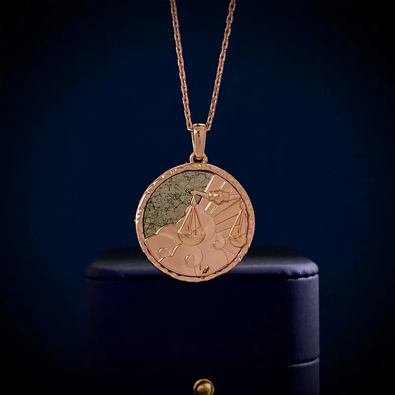 A gold zodiac necklace with an engraved circular medallion featuring clouds and a set of scales, displayed against a dark blue background atop a dark jewelry box—an elegant piece of astrology jewelry.