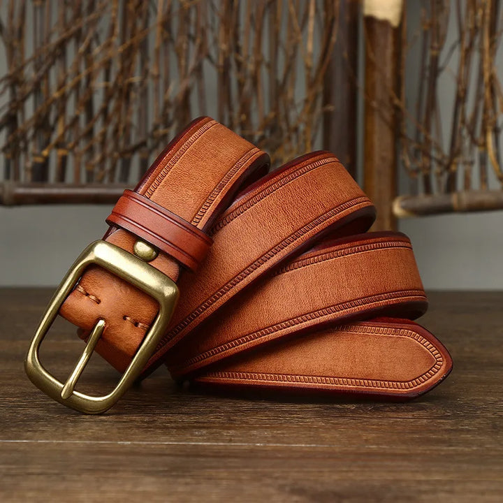 A genuine leather brown belt with a brass buckle is coiled on a wooden surface, with decorative twigs in the background.