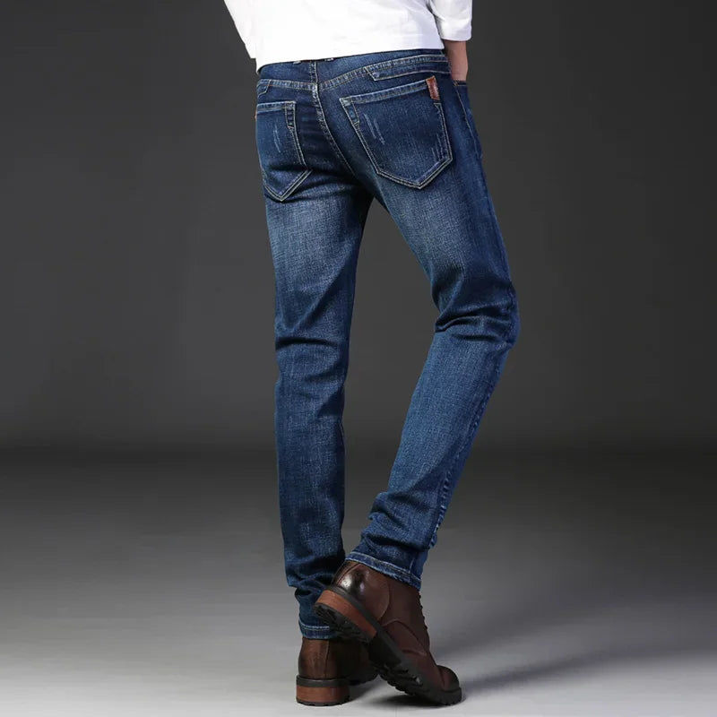A person wearing slim-fit jeans made from durable fabric and brown leather shoes stands with their back to the camera against a dark, plain background. Only their legs and lower torso are visible.
