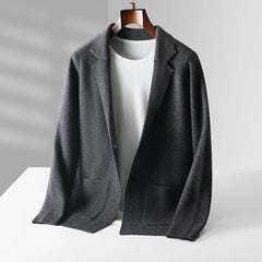 A dark gray business casual cardigan with front pockets is draped over a white crewneck t-shirt on a wooden hanger, displayed on a white surface with soft natural light and shadows in the background.