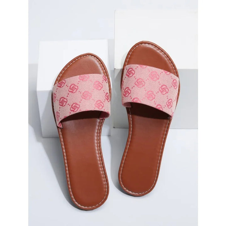 A pair of modern slippers with open toes, brown soles, and wide pink fabric straps featuring a repeating interlocking logo pattern in red. Perfect for summer, these sandals are displayed on a white background with geometric props.