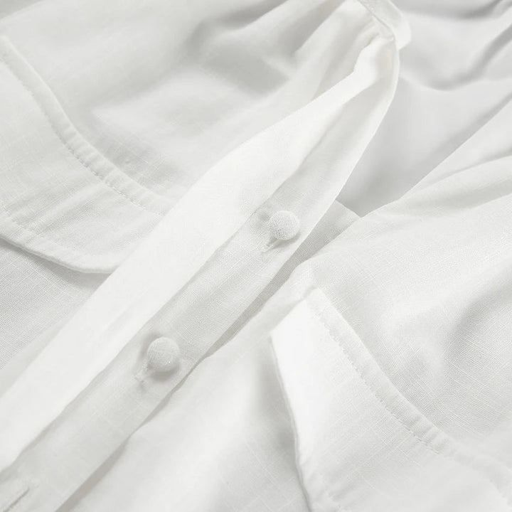 Close-up of a white linen shirt showing fabric texture, front buttons covered in matching fabric, and two chest pockets with visible stitching details—a streetwear staple perfect for a relaxed summer outing.