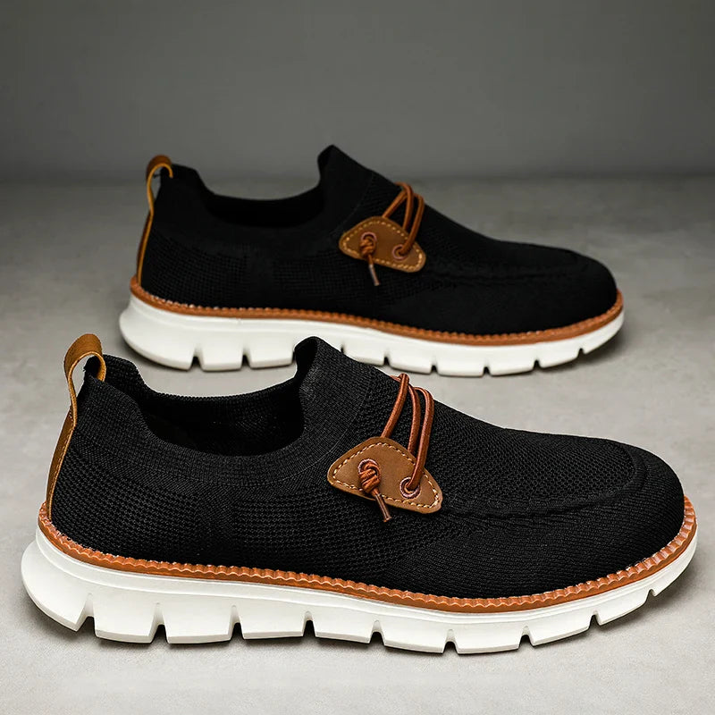 A pair of black slip-on sneakers with white chunky soles, brown stitching, brown leather accents, and brown laces, displayed on a neutral background—these breathable loafers offer both comfort and stylish detail.