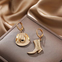 A pair of gold hoop earrings, one with a cowboy hat charm and the other with a cowboy boot charm, displayed on a brown jewelry box—perfect western jewelry for those who love unique cowgirl accessories.