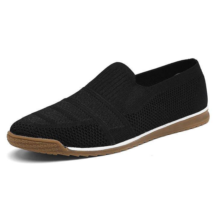 Black slip-on men's casual shoes with a breathable knitted texture, brown rubber sole, white midsole accent, and a low-profile design, shown on a white background.