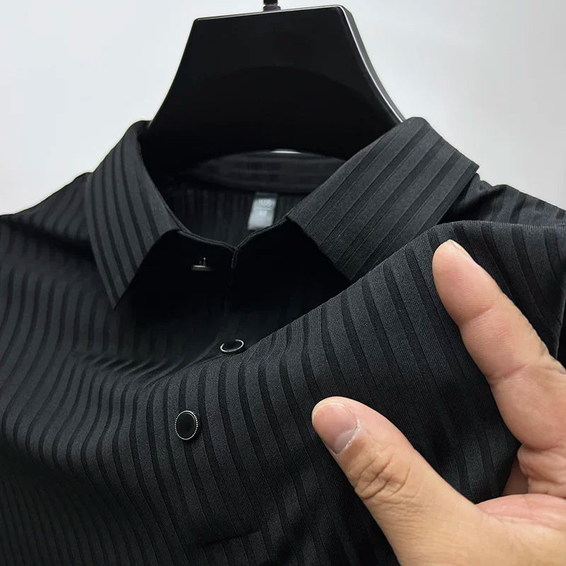 A hand holds the collar of a black, vertically striped dress shirt made from luxurious silk fabric on a black hanger against a plain light background.