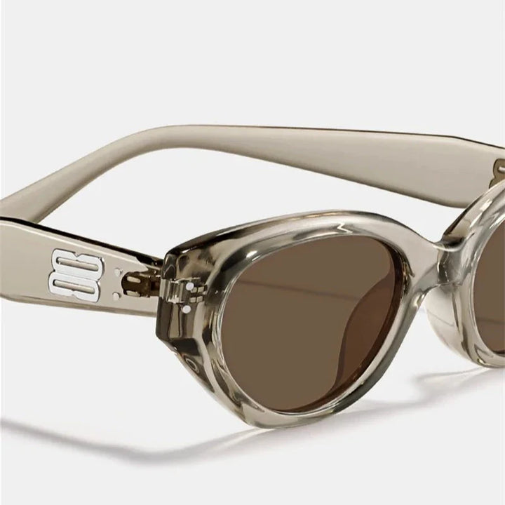 Close-up of stylish, oval-shaped sunglasses with thick, translucent acetate frames and dark tinted, scratch-resistant lenses, featuring a silver decorative detail on the temple.