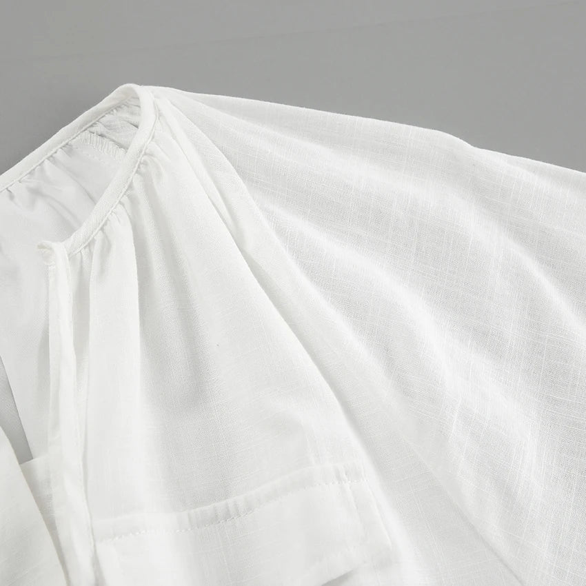 A close-up of a white, lightweight, semi-sheer blouse with a subtle texture—perfect for a summer outing—featuring a gathered neckline and a visible pocket on the front. The fabric appears soft and airy.
