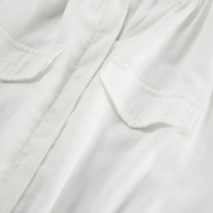 Close-up of a white shirt made from lightweight fabric, showing two chest pockets with flaps and a central placket—ideal for streetwear or layering over a chic romper on your next summer outing. The fabric has a subtle texture and a slightly sheer appearance.