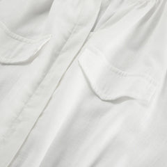 Close-up of a white shirt made from lightweight fabric, showing two chest pockets with flaps and a central placket—ideal for streetwear or layering over a chic romper on your next summer outing. The fabric has a subtle texture and a slightly sheer appearance.