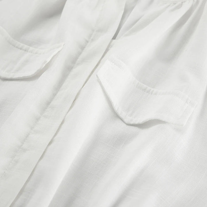 Close-up of a white shirt made from lightweight fabric, showing two chest pockets with flaps and a central placket—ideal for streetwear or layering over a chic romper on your next summer outing. The fabric has a subtle texture and a slightly sheer appearance.