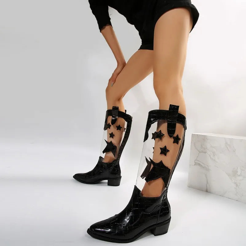 A person wearing mid-calf clear panel boots with black star and butterfly cutouts, crafted from glossy faux-crocodile leather, stands against a white background.