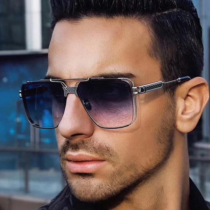 A man with short dark hair and trimmed facial hair wears vintage sunglasses with silver frames and gradient lenses, offering UV400 protection as he looks off to the side outdoors.