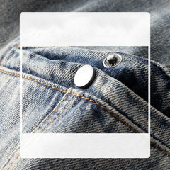 Close-up of classic fit blue denim jeans pocket with visible stitching and two metal rivets, one silver and one black, highlighting the stone washed texture and detail of the fabric.