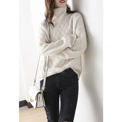A woman leans against a white wall, wearing an ultra soft, cream-colored turtleneck sweater with a textured knit pattern, black ripped jeans, and carrying a small white shoulder bag. Her face is partially turned away.