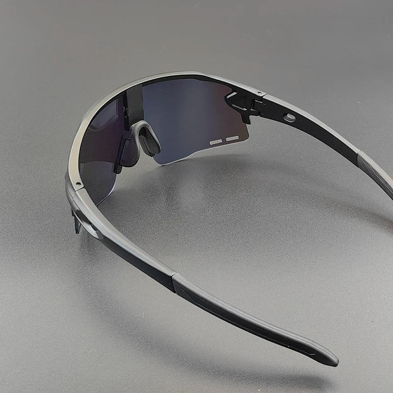 A pair of black sports sunglasses with dark, semi-rimless polarized lenses is placed on a smooth, gray surface. The arms and nose pads are visible, and the frame has a modern, angular design.