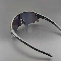 A pair of black sports sunglasses with dark, semi-rimless polarized lenses is placed on a smooth, gray surface. The arms and nose pads are visible, and the frame has a modern, angular design.