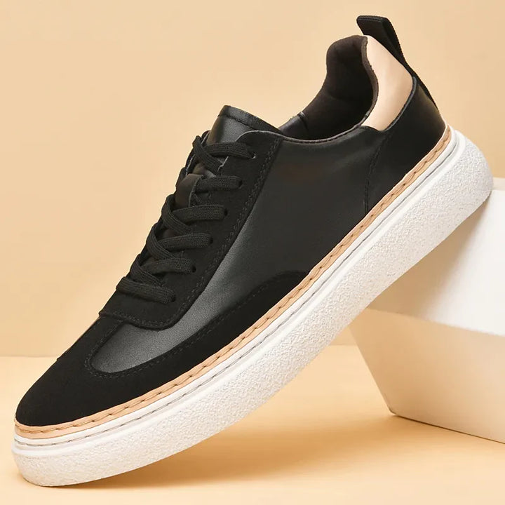A black sneaker with black laces, a white textured sole, and a light beige accent on the heel, featuring a cushioned insole for added comfort, displayed against a tan background.