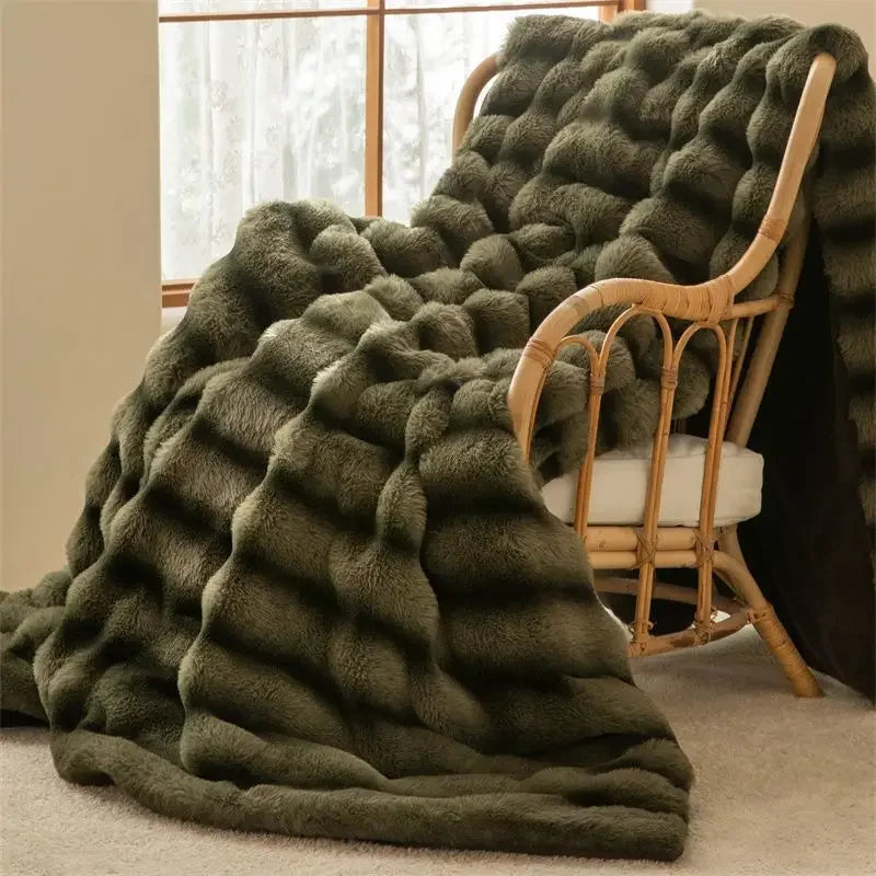 A plush, dark green luxurious throw with an elegant wave pattern drapes over a light-colored cushioned rattan chair next to a window, creating a cozy and inviting atmosphere in the room.
