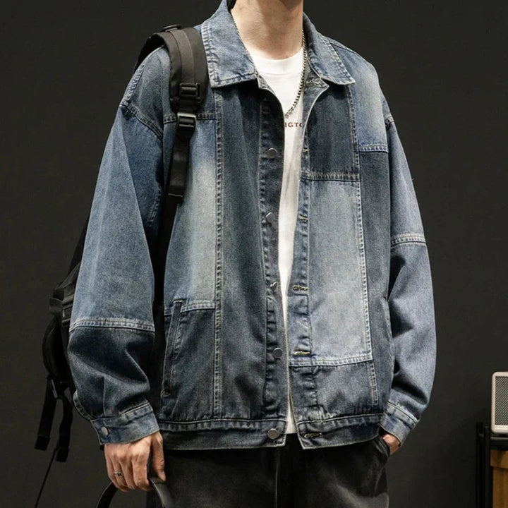 A person wearing an oversized fit, denim patchwork jacket over a white t-shirt, with black jeans and a black backpack, stands against a dark background for a retro style look.